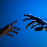 A human hand and a metallic robotic hand reaching toward each other against a deep blue background, fingertips almost touching