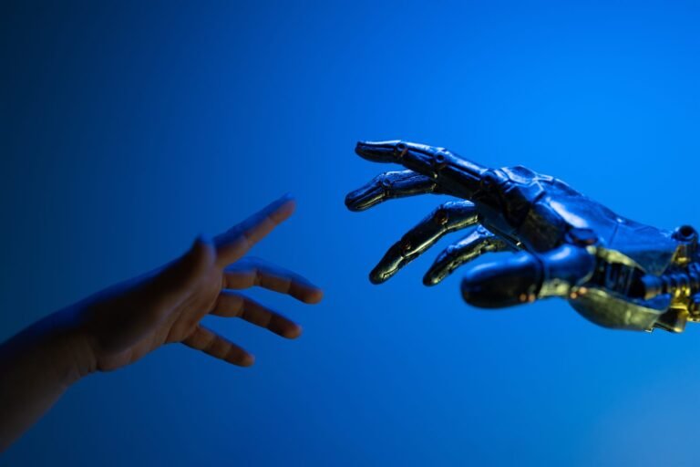 A human hand and a metallic robotic hand reaching toward each other against a deep blue background, fingertips almost touching